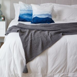knitted blanket with tassles on a white bed linen with blue sea colour cushions