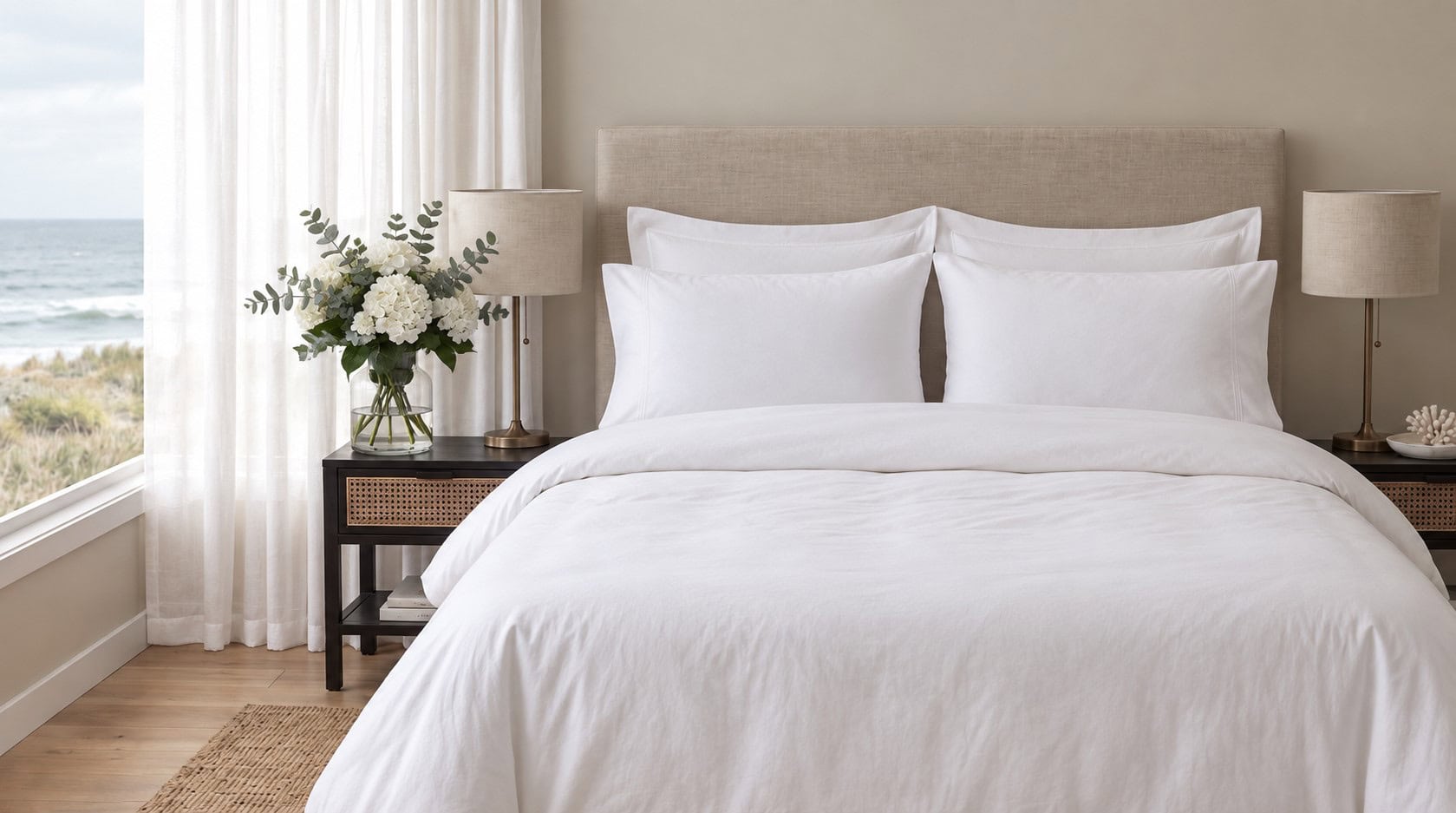 200 Thread Count 100% Cotton Percale Duvet Cover Set - White, Grey & Duck Egg 1 A neatly made bed dressed in crisp white linens, featuring four pillows and a white duvet, set against a beige upholstered headboard in a bright, coastal-style bedroom with dark wood nightstands.